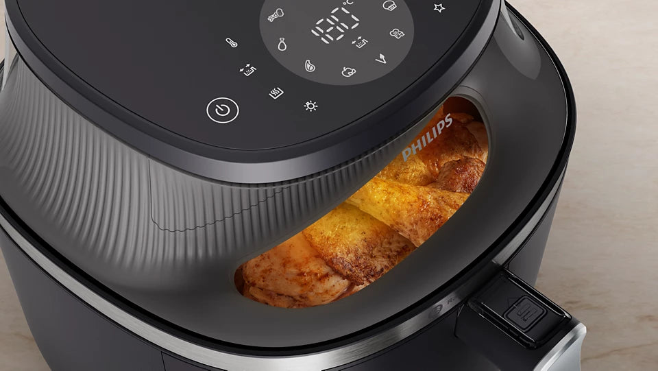 Bovenaanzicht van een open Ninja Airfryer MAX PRO met een hele geroosterde kip en aardappeltjes in de mand. Een persoon haalt de lade eruit, wat illustreert dat de 6,2 liter mand ruimte biedt aan een royale portie (bijvoorbeeld een hele kip).